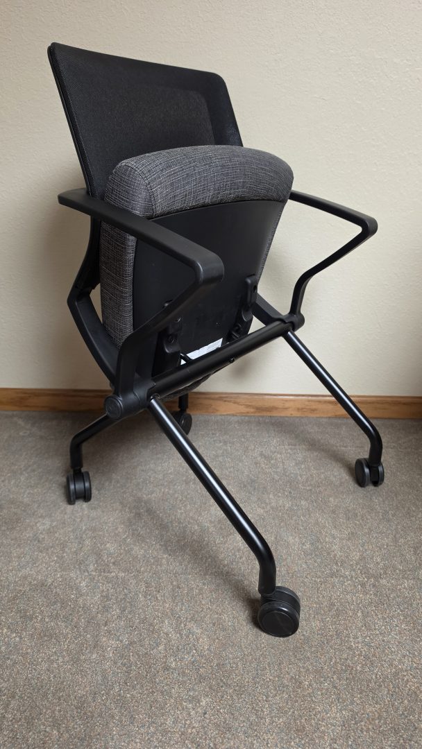 A mobile training room chair shown with the seat flipped up, demonstrating its space-saving nesting design.
